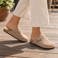 Mujer caminando con zuecos mule de ante beige en una terraza de madera