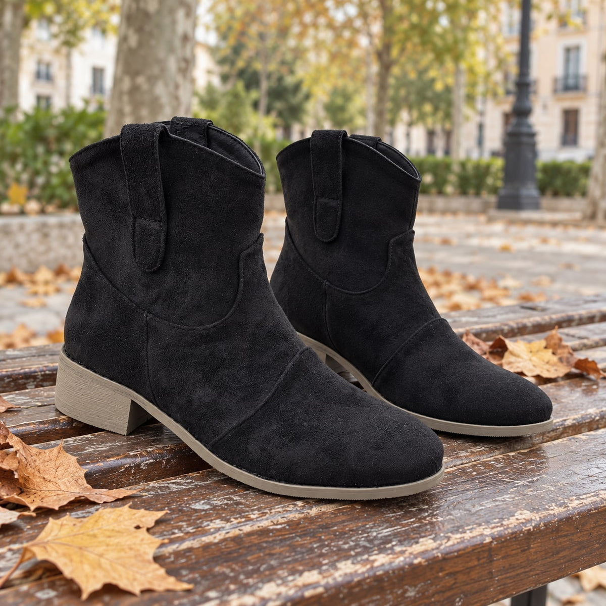 Botines cowboy negros de efecto ante sobre un banco de madera con hojas de otoño