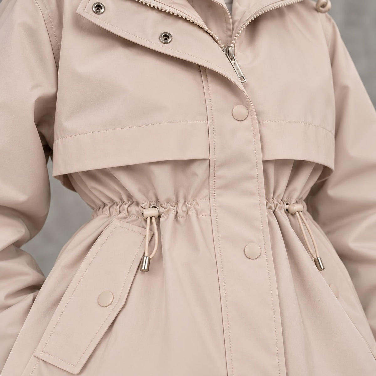 Detalle de cordón de cintura, botones y tejido de parka beige