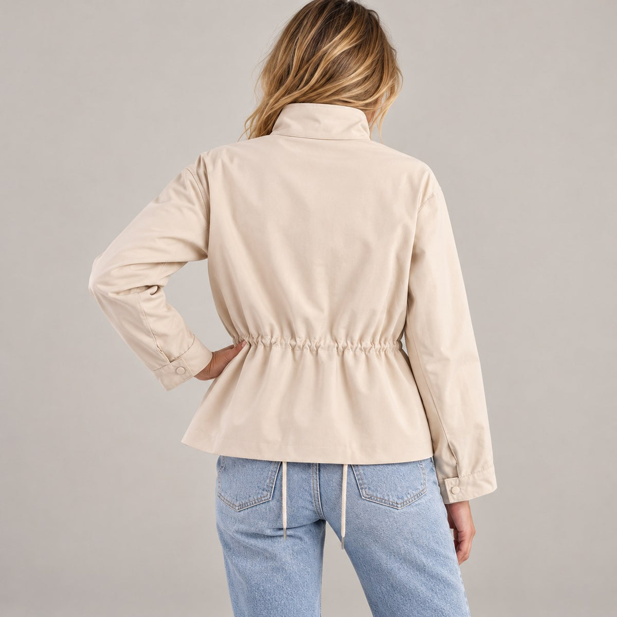 Chaqueta entretiempo beige de espaldas con la mano en la cadera