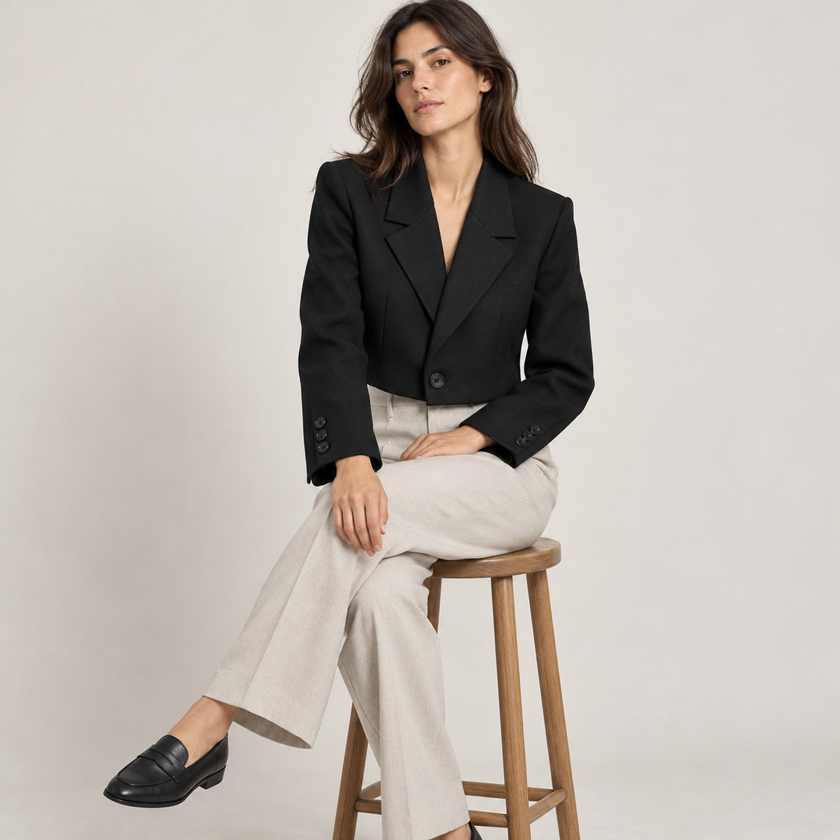 Blazer recto negro abrochado, sentada en estudio con pantalón claro