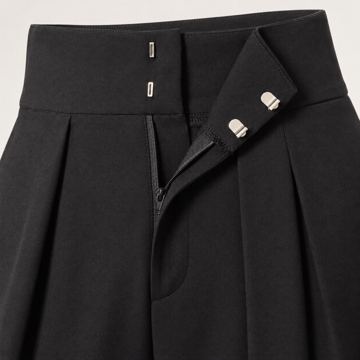 Detalle de la pretina, los corchetes y los pliegues del pantalón globo negro