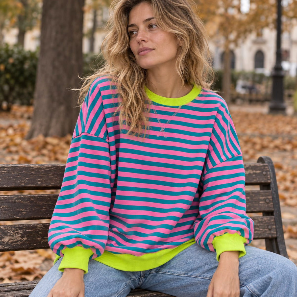 Jersey oversize de rayas rosa y turquesa con ribetes verde lima junto a un banco urbano