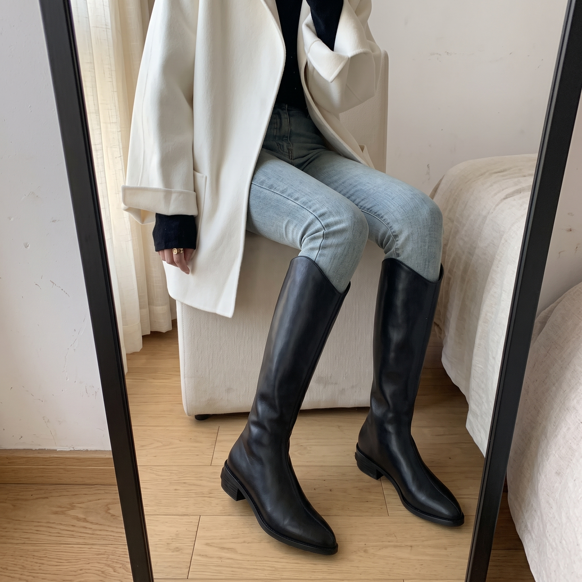 Botas altas negras con costura central puestas con vaqueros, foto real en casa