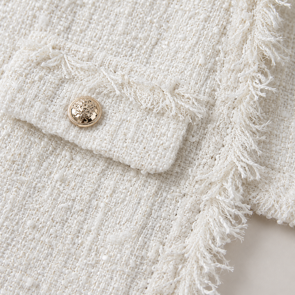 Primer plano del tejido tweed blanco con flecos y botón dorado